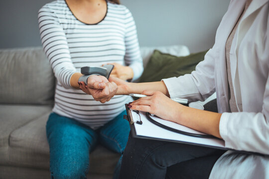 Doctor measuring blood pressure of young pregnant woman, close up. Eclampsia of pregnant women concept. Young doctor is checking blood pressure of pregnant woman at home. 