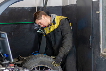 Obraz na płótnie Canvas Young mechanician changing car wheel in auto repair shop using equipment