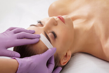 Beautician is removing hair from beautiful female face with hot wax. Woman has a beauty treament...