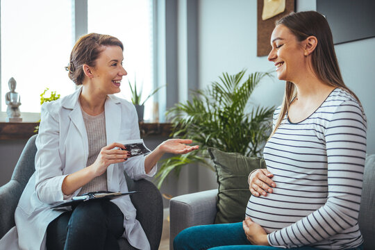 Young  woman smiles while looking at her baby's ultrasound image. She is meeting with a home healthcare nurse. Pregnant woman and doctor looking at her baby ultrasound picture..