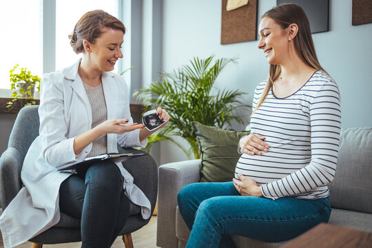 Young  woman smiles while looking at her baby's ultrasound image. She is meeting with a home healthcare nurse. Pregnant woman and doctor looking at her baby ultrasound picture..