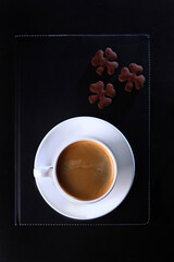 A white coffee cup and a black leather-bound notebook.Flat lay.Top view.Copy space.Food and drinks.Coffee break.Cookies in the shape of a clover.