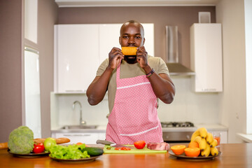 African man in an apron preparing food in the kitchen eating an ear of corn