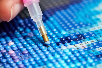 Girl collect diamond painting. Diamond embroidery with a tweezers. Acrylic rhinestones. Close-up, selective focus.