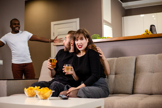 The black man extended his arms to the side in greeting to his friends. Couple meeting with an African friend. Hanging out with friends on the couch with beer and chips