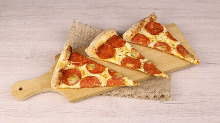 Three slices of pepperoni pizza on a wooden cutting board