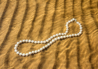 Pearl beads lie on the sand in the water of the bay