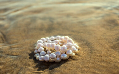 Fototapeta na wymiar Pearl beads lie on the sand in the water of the bay