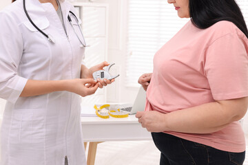 Overweight woman and nutritionist with digital caliper in clinic, closeup