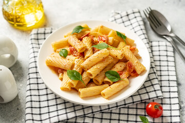 Tortiglioni with tomatoes, ricotta and basil in a white plate on a light kitchen table. Traditional Italian pasta with vegetables and creamy cottage cheese in a bowl closeup