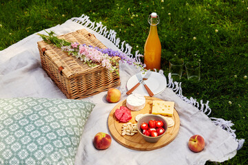 leisure and drinks concept - close up of food, drinks and basket on picnic blanket on grass