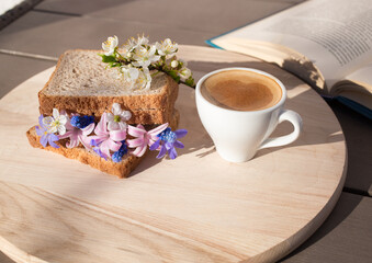 Obraz na płótnie Canvas sandwich with spring flowers between slices of toast, a cup of coffee and a book is a wonderful healthy breakfast. good morning, flower fantasies, positive atmosphere, flora inspiration. Hi spring