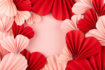 Valentines day background - many gentle pink and red hearts of chinese paper fans on pastel pink color as frame with copy space for design, card, text, advertising, top view.