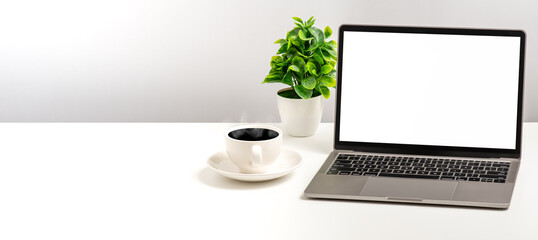 Fototapeta premium Empty white screen laptop, coffee cup, and vase placed on a white desk in the office. The concept for business, technology, internet. copy space on left. Close up, selective focus, white background