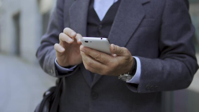 Man in business suit scrolling web pages on smartphone, booking taxi, ordering food delivery in online application, reading news waiting for bus outdoor, checking e-mail and replying to letters