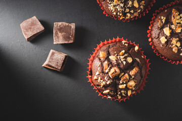 Homemade chocolate muffins or cupcakes sprinkled of nuts on dark background, top view