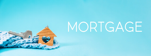 Web banner of mortgage. Close-up of a key and small keychain wooden house with a heart lying in a...
