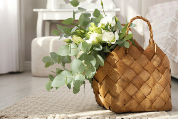 Stylish wicker basket with bouquet on floor in bedroom