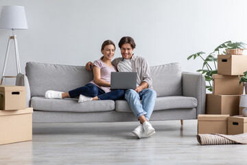 Fototapeta na wymiar Busy happy european young man show computer to woman on sofa in living room interior