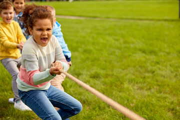 childhood, leisure and people concept - group of happy kids playing tug-of-war game and running at...