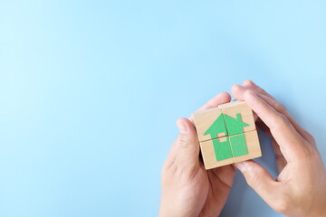 Human hand putting together house icon puzzle made of wooden blocks. Property real estate...