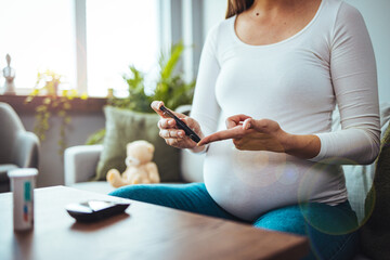 Happy Pregnant woman with glucometer checking blood sugar level at home. Woman testing for high blood sugar. Pregnant Woman holding device for measuring blood sugar...
