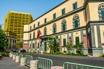 Obraz premium Tirana, Albania - June 21, 2021: Building of the Ministry of Transport and Infrastructure on Skanderbeg Square in Tirana. Decorated house with a yellow facade and green wooden shutters on the windows