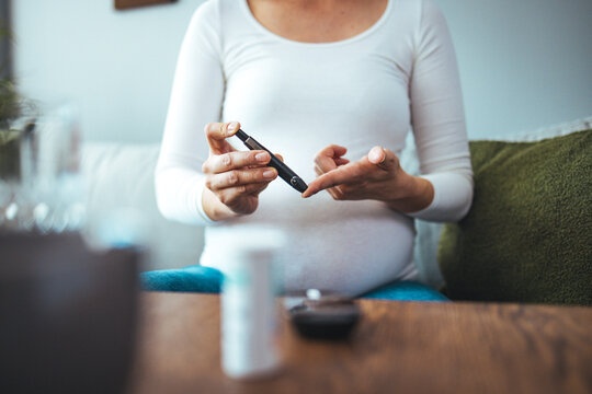 Pregnancy, health and glycemia concept - pregnant beautiful woman checking blood sugar level with glucometer and lancing device at home