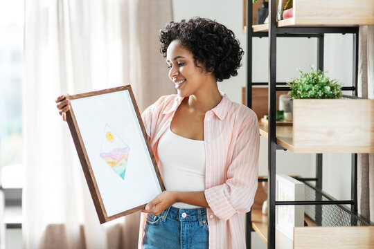home improvement, decoration and people concept - happy smiling woman holding abstract watercolor picture in frame at shelf
