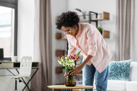 household, home improvement and interior concept - happy smiling young woman placing flowers on coffee table