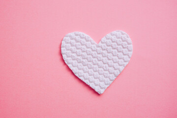 White fabric heart on pink table, top view.