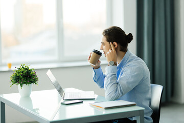 Young businessman using computer and drinking coffee in office. Handsome man on coffee break