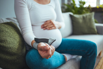 Pregnant woman measuring blood pressure, health check of expecting mom. She checking blood pressure at home. High pressure problem during pregnancy concept.