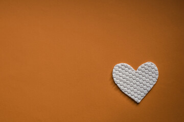 White fabric heart on carrot brown table. Art card