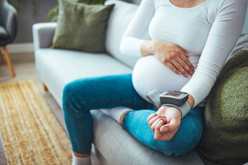 Frontal close-up of a pregnant woman's abdomen, measures blood pressure with a sphygmomanometer,...