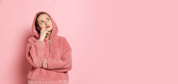 Dreams. Half-length portrait of young woman, student with short hair in pearch color hoodie isolated on pink background. Concept of emotions, studying, ad
