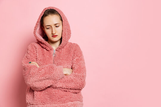 Sad young woman, student with short hair in pearch color hoodie isolated on pink background. Concept of emotions, studying, ad