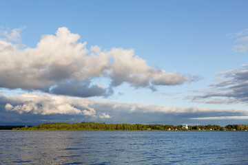 Scenic view on the calm Volga river with forest on horizon. Fluffy clouds reflected in mirrorlike glossy water. Summer, Volga, Tver region, Russia