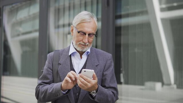 Adult man in stylish eyeglasses reading message with good news on smartphone