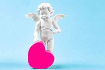Cherub baby and pink heart on blue background. White cupid standing figurine, Valentines day...
