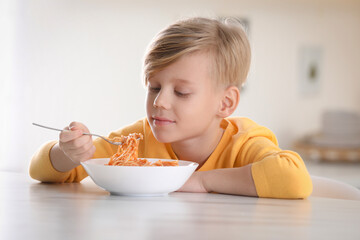 Cute boy eating tasty pasta at table in kitchen