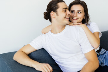 Fototapeta premium Happy young couple of man and woman embracing look at each other sitting on couch in living room.