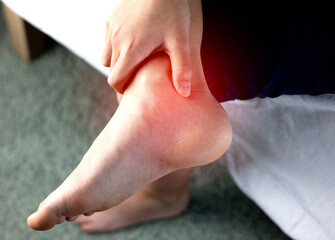 A person holding ankle on Achilles tendon, suffering with pain in red spot area. Sprain ligament or...