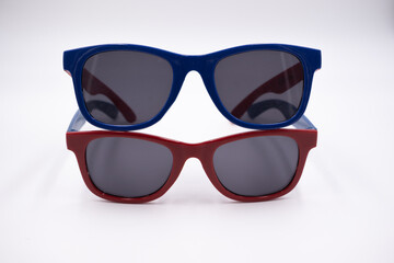 Two children's sunglasses with red and blue frames standing on top of each other isolated on white...