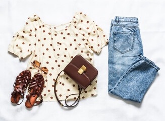 Set of women's summer clothes - blue mom jeans, polka dot blouse, sandals  and  cross body bag on a light background, top view