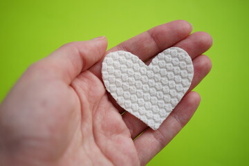 Hand with white fabric heart on vivid green background