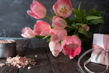 Lovely gifts for mothers day. Atmospheric still life with pink tulips and gifts for wellness on dark vintage wood. Background with short depth of field.