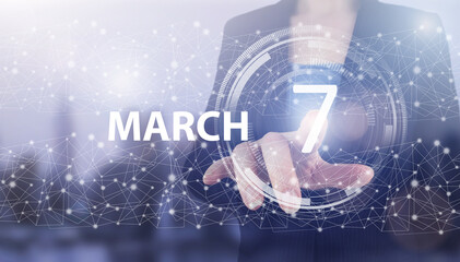 March 7th. Day 7 of month, Calendar date. Hand click luminous hologram calendar date on light blue town background. Spring month, day of the year concept.