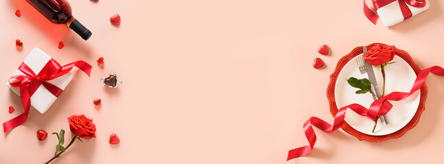 Valentines day banner with gift, red roses, hearts wine and table place setting on pink background. View from above. Greeting card. Invitation to romantic dinner.