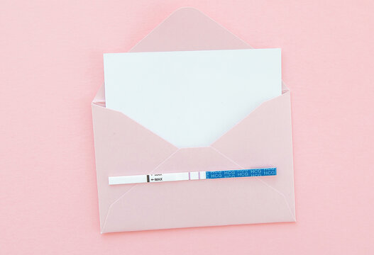 positive pregnancy test in pink envelope on pink background, postcard with place for text, pregnancy concept.